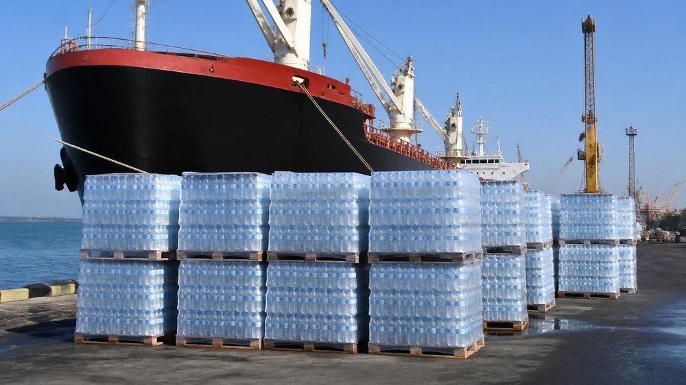 Pallets of bottled drinking water on the quay beside a cargo ship